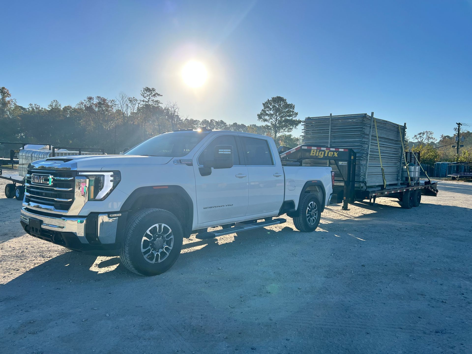 White pickup truck towing a flatbed trailer in a sunny gravel lot
