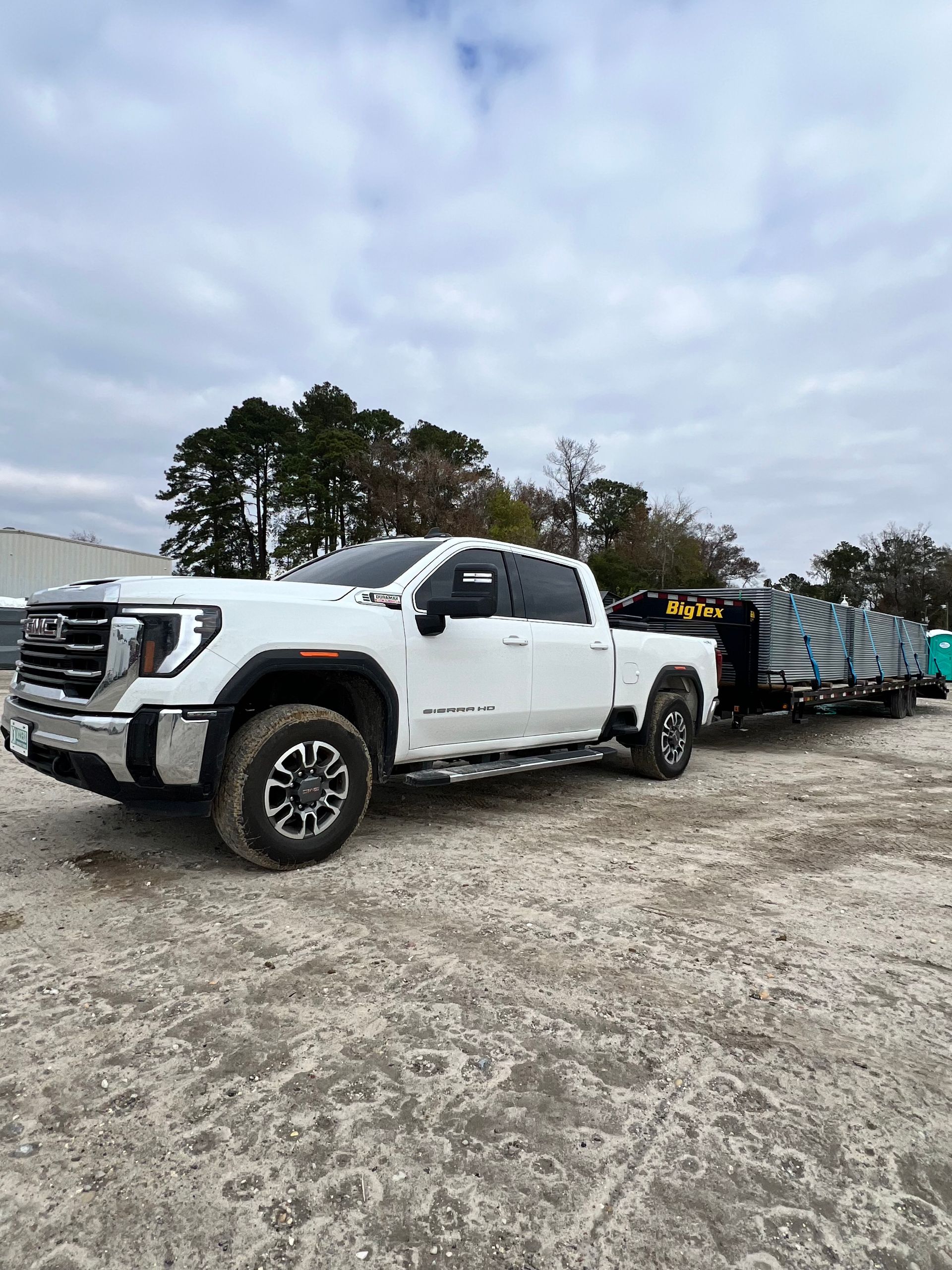 White pickup truck towing a flatbed trailer on a gravel lot under cloudy skies