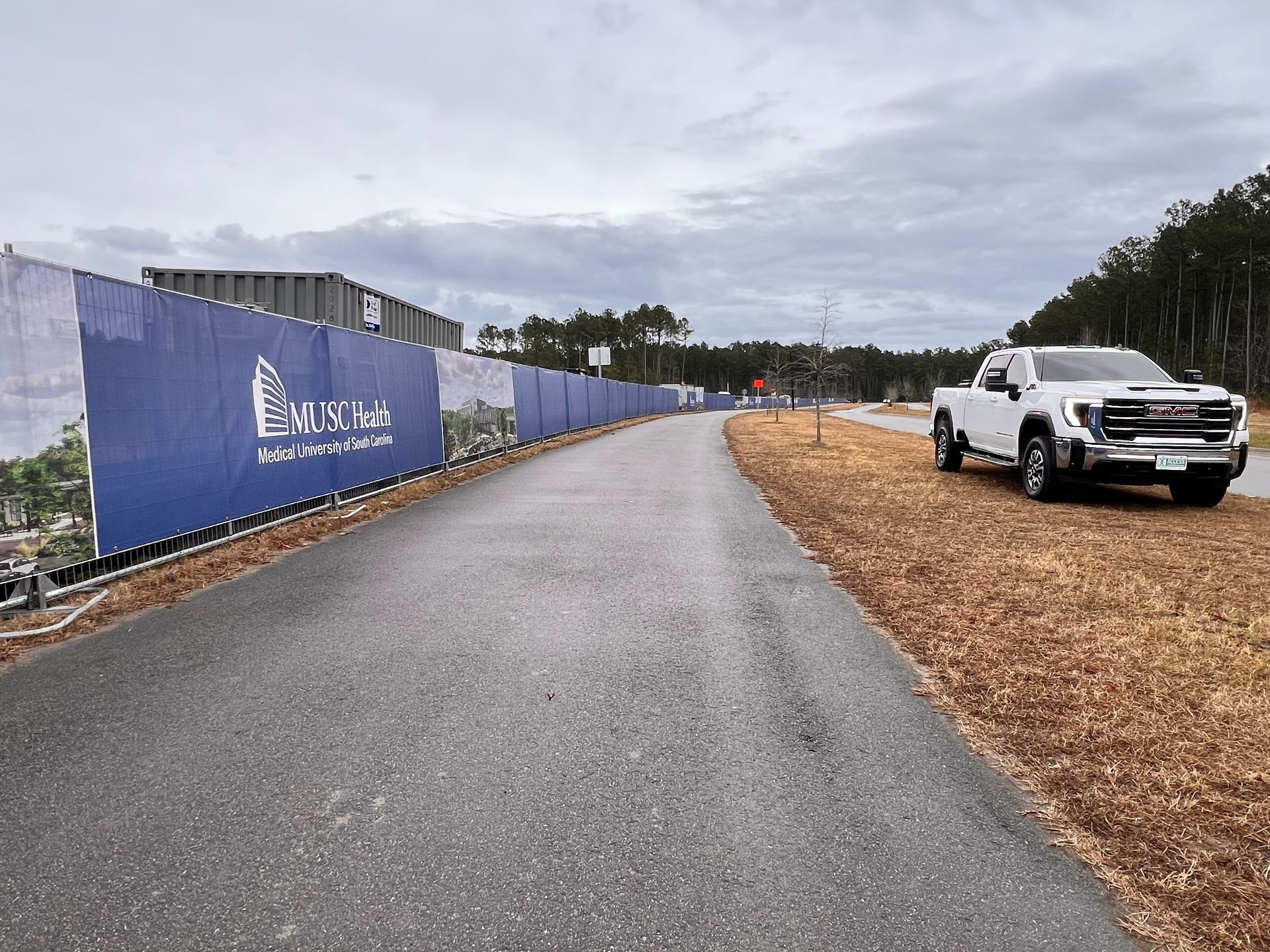 Roadside construction area with blue fence, paved path, and white pickup truck on the right.