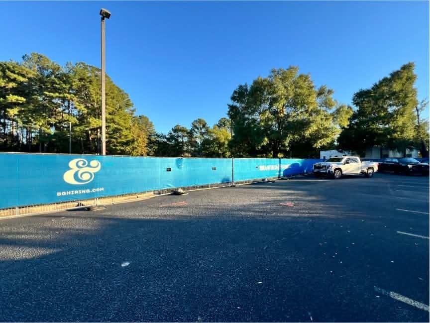 Blue wall with white logo in a sunny parking lot, with parked cars and trees in the background