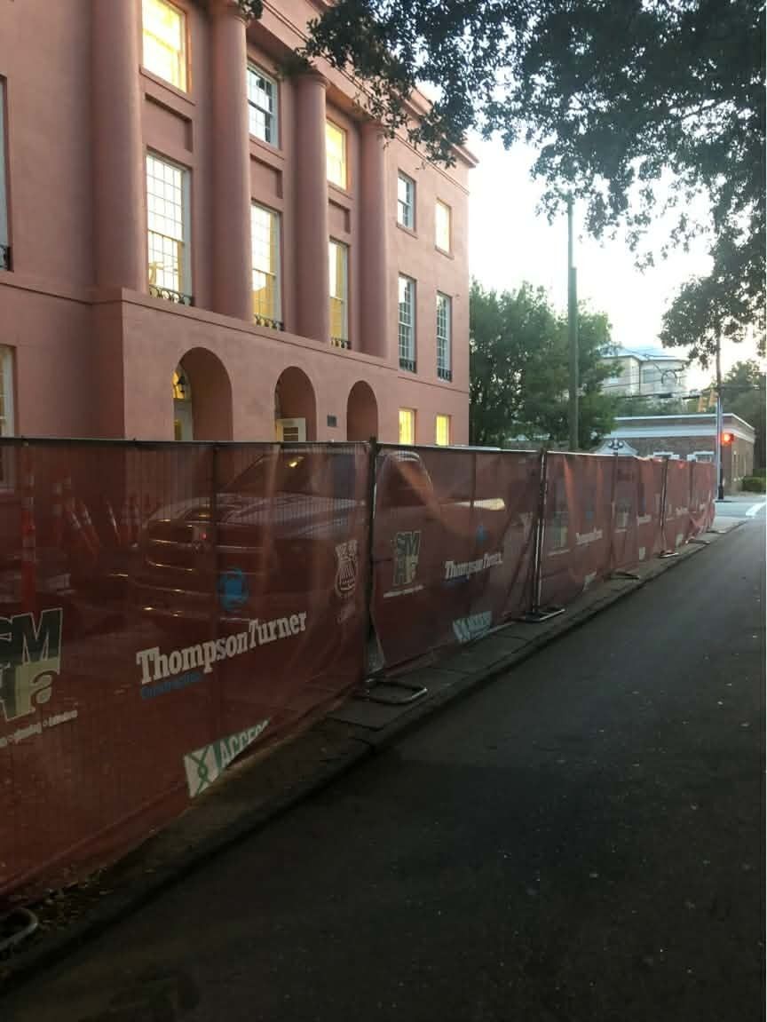 Red construction barrier along a street beside a pink brick building with arched windows at dusk