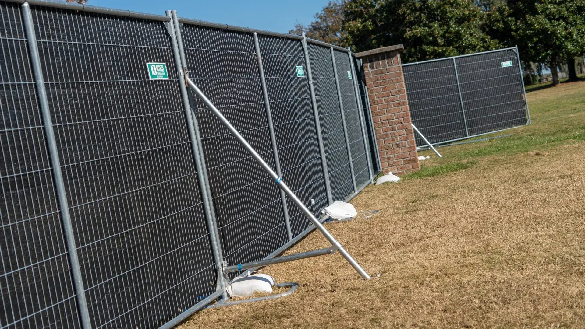 Chain-link fence with black privacy panels along a grassy outdoor area, held by white support poles.