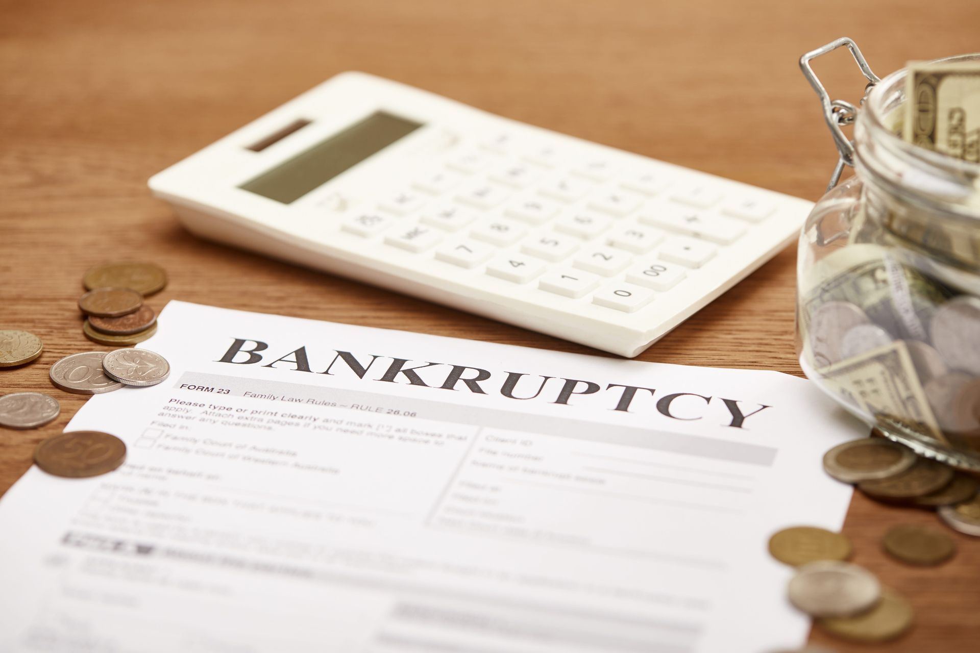 Bankruptcy form beside calculator and scattered coins on a wooden desk