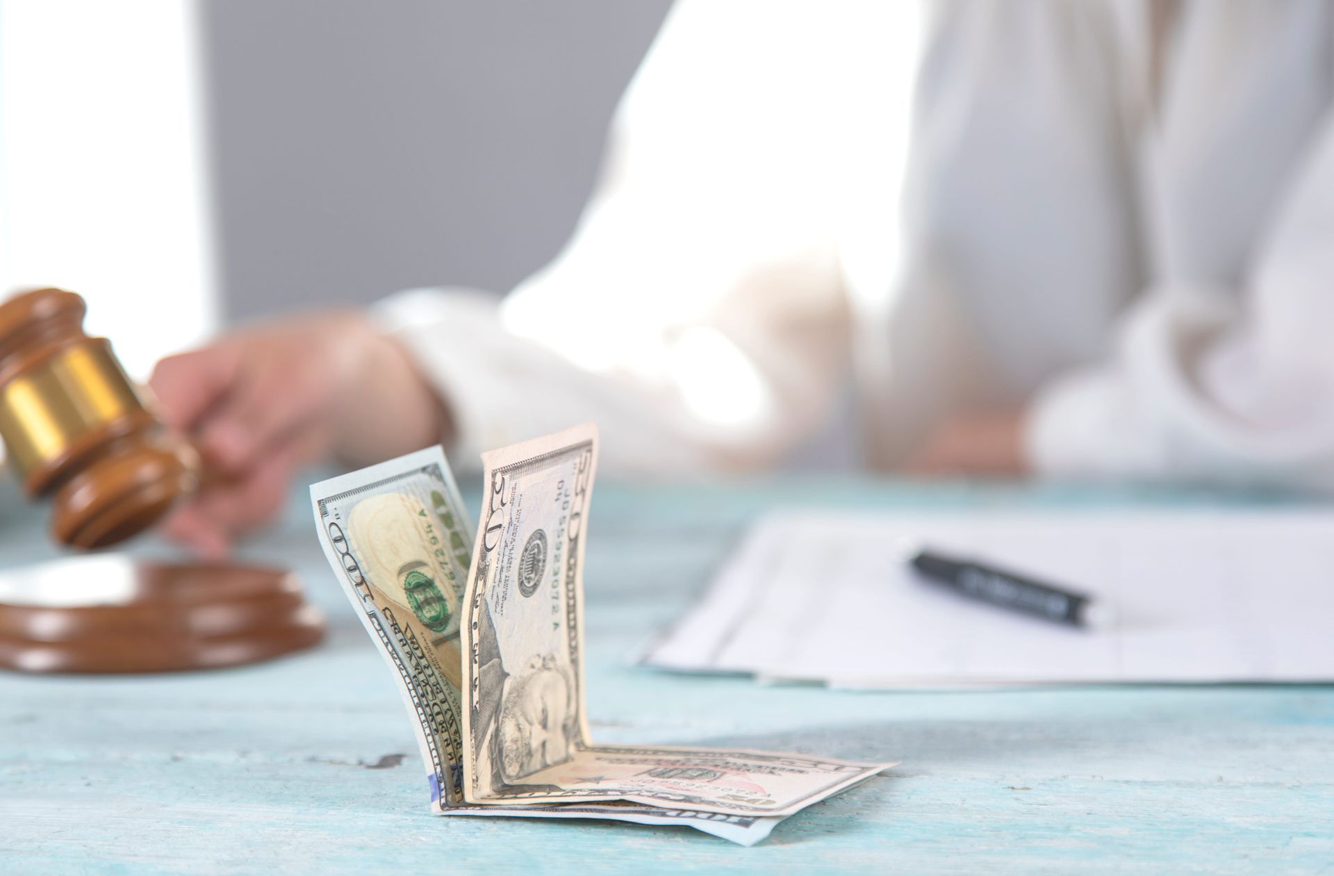 Judge’s gavel beside folded dollar bills on a desk, with paperwork and a pen in the background.
