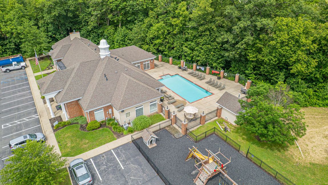 Aerial view of a community center with a pool, playground, and parking lot surrounded by trees.