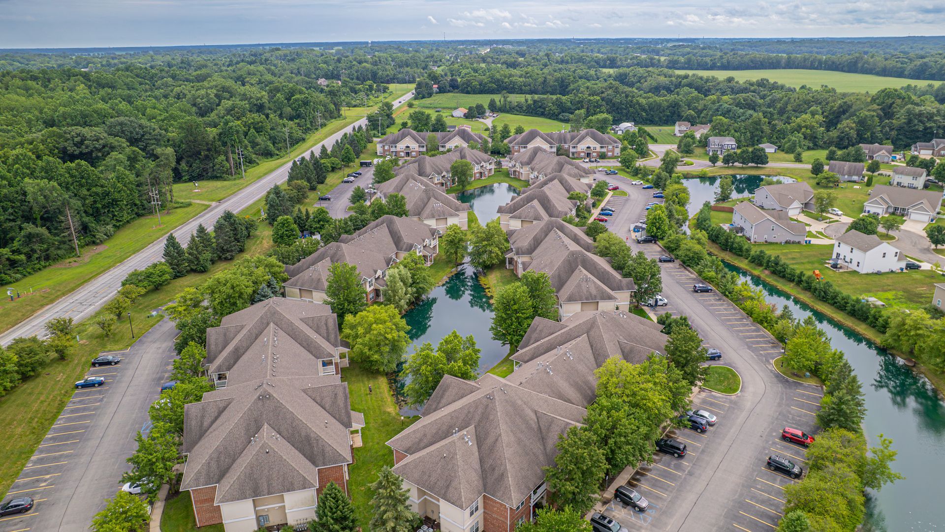 Aerial view of a residential area with brown-roofed buildings surrounding a blue lake, trees, and roads.