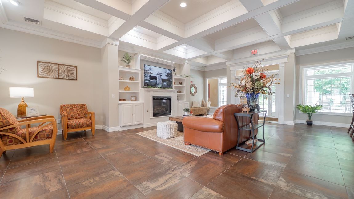 Lounge area with fireplace, TV, and seating. Beige walls, brown floors, white ceiling beams.