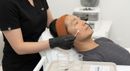 Aesthetic treatment in a clinic, with a masked practitioner applying a facial device to a patient