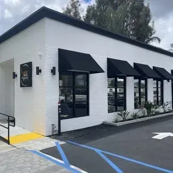 White storefront with black awnings and windows, seen from a parking lot with blue handicap lines.