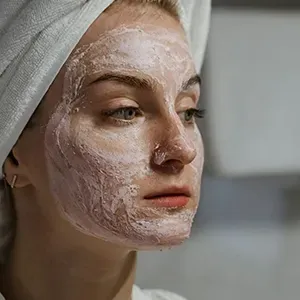 Woman with a white facial mask and towel wrapped around her head in a spa setting