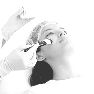 Facial treatment being applied with a brush while a person lies on a treatment bed