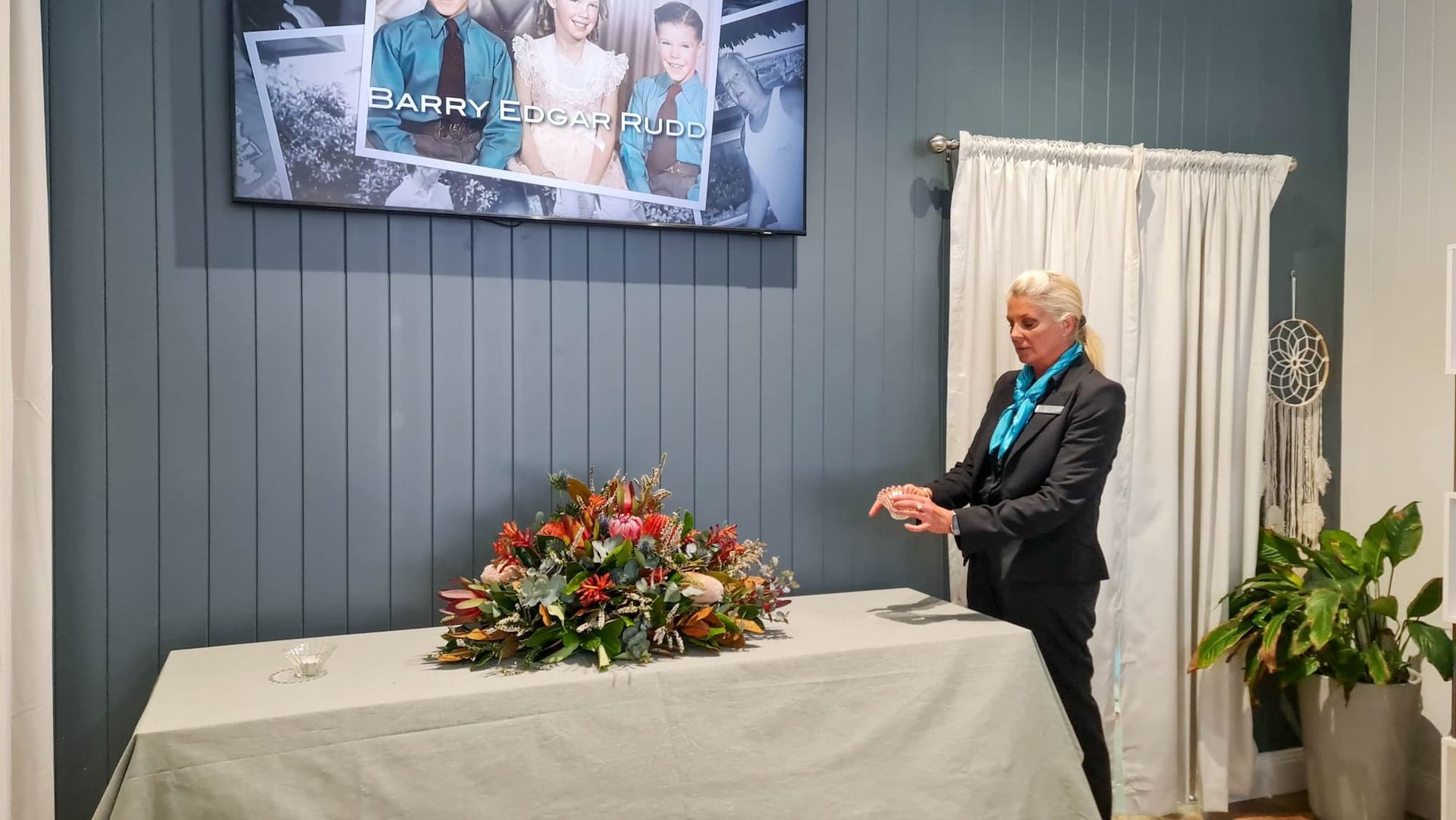 A Funeral Director Placing a Small Glass Bowl on a Table With a Decorative Floral Arrangement — Personalised Cremation Services in The Entrance, NSW