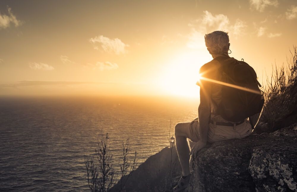 Man sitting on the rock at sunset — Personalised Cremation Services in The Entrance, NSW