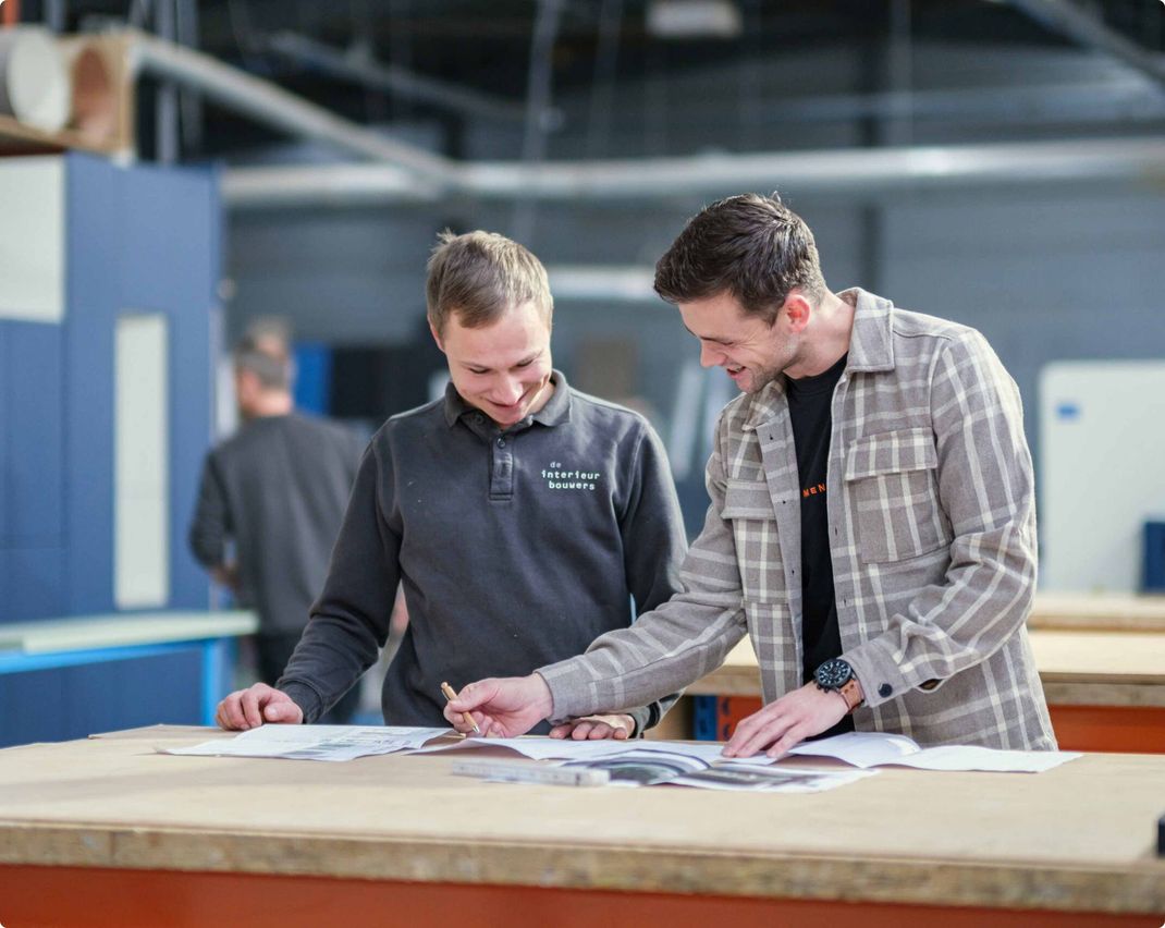 Two men are looking at a piece of paper on a table.