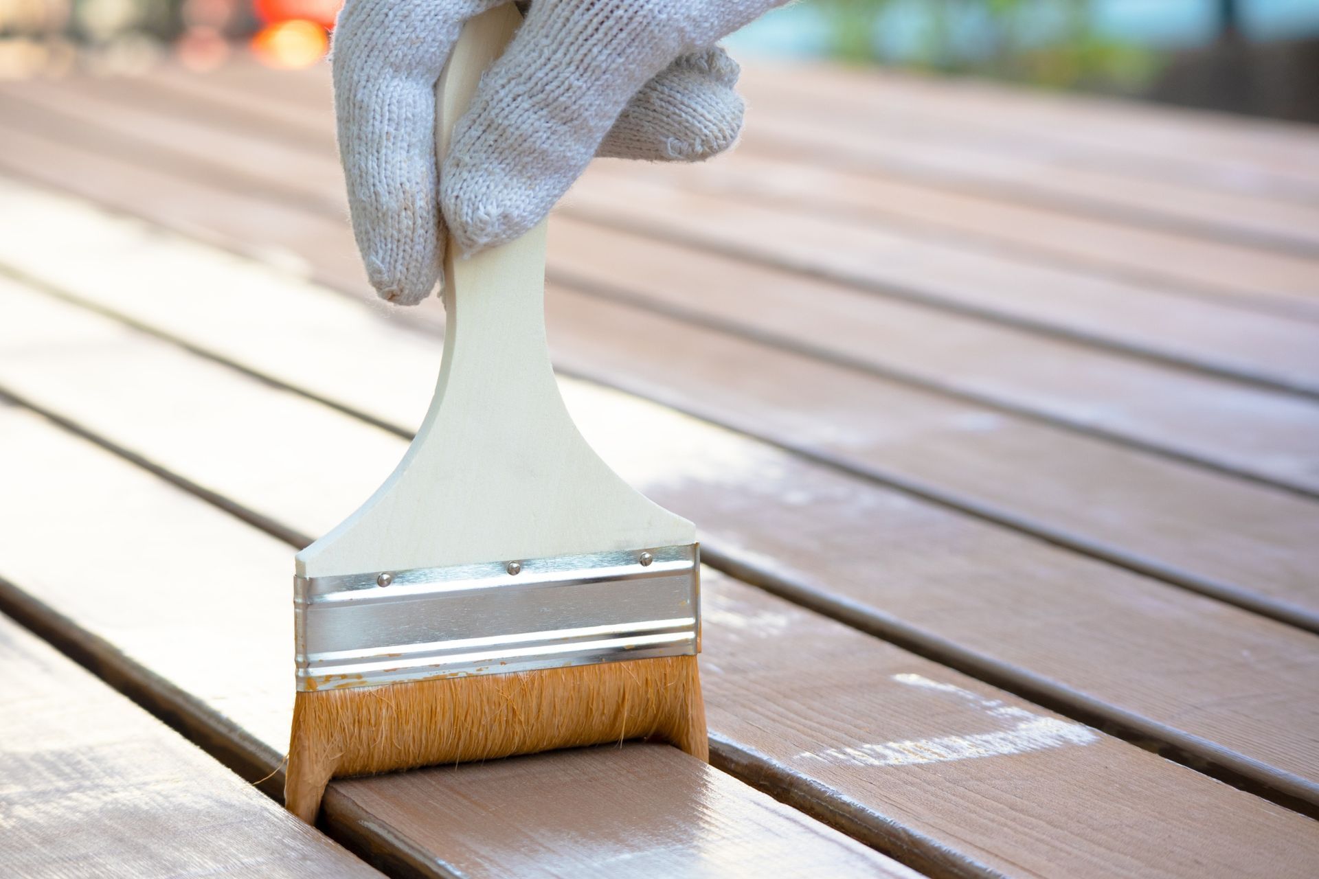 Gloved hand painting a wooden deck with a brush