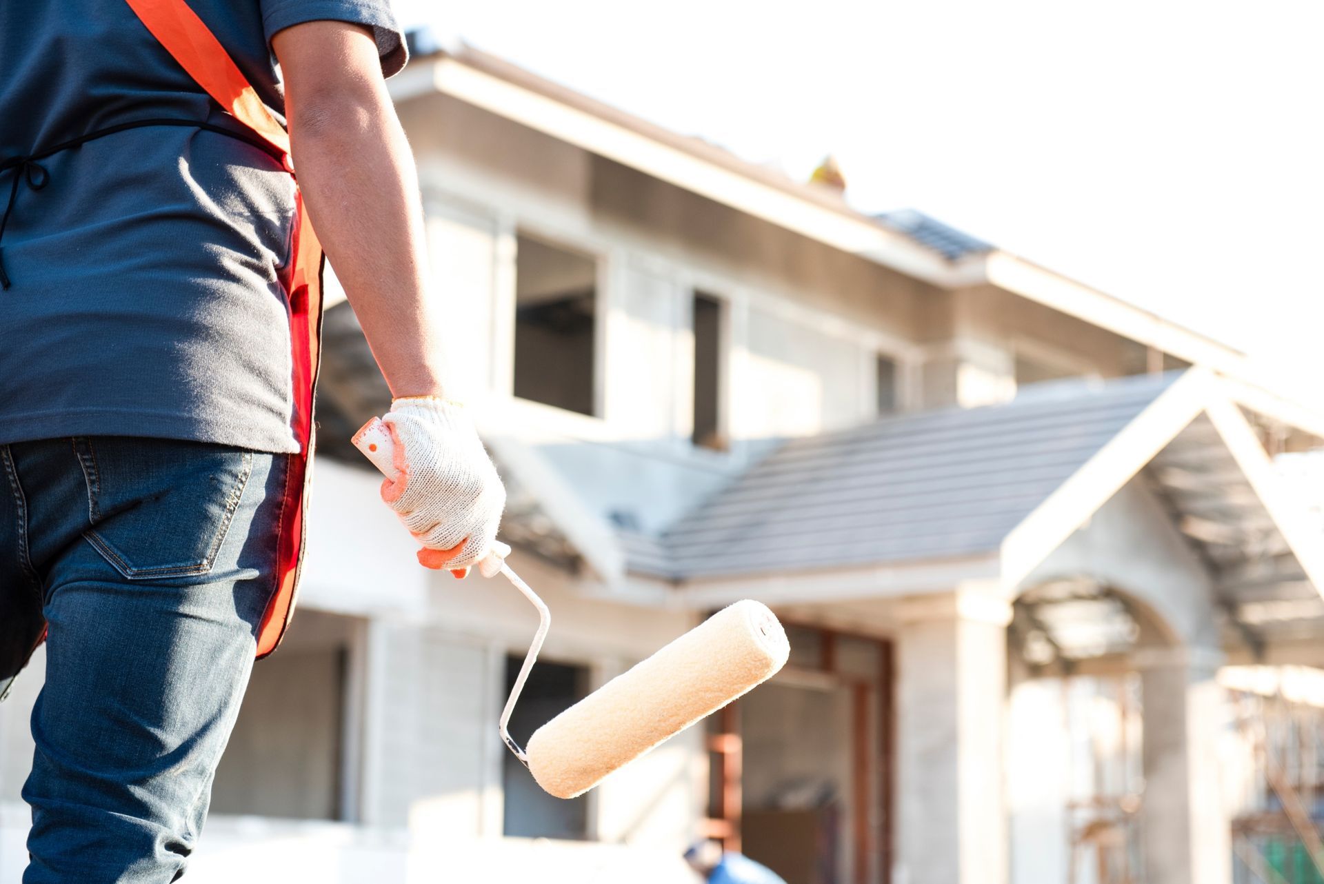 Person painting a house exterior with a roller on a sunny day