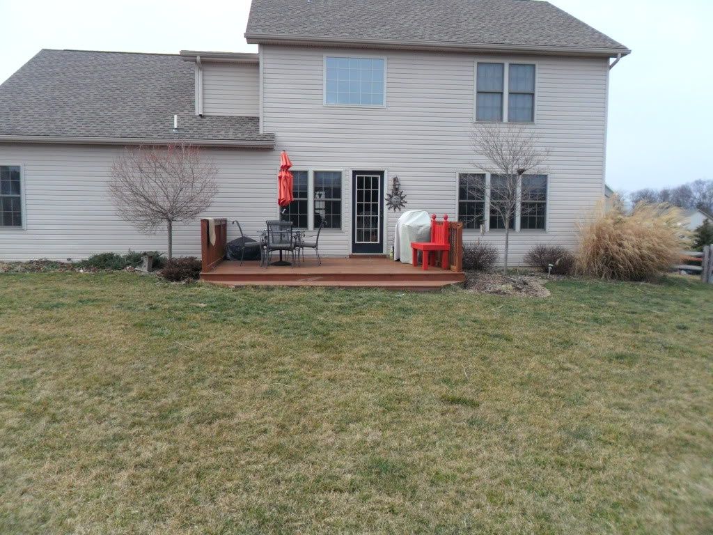 Backyard deck with patio furniture, red umbrella, and sliding glass doors on a beige house