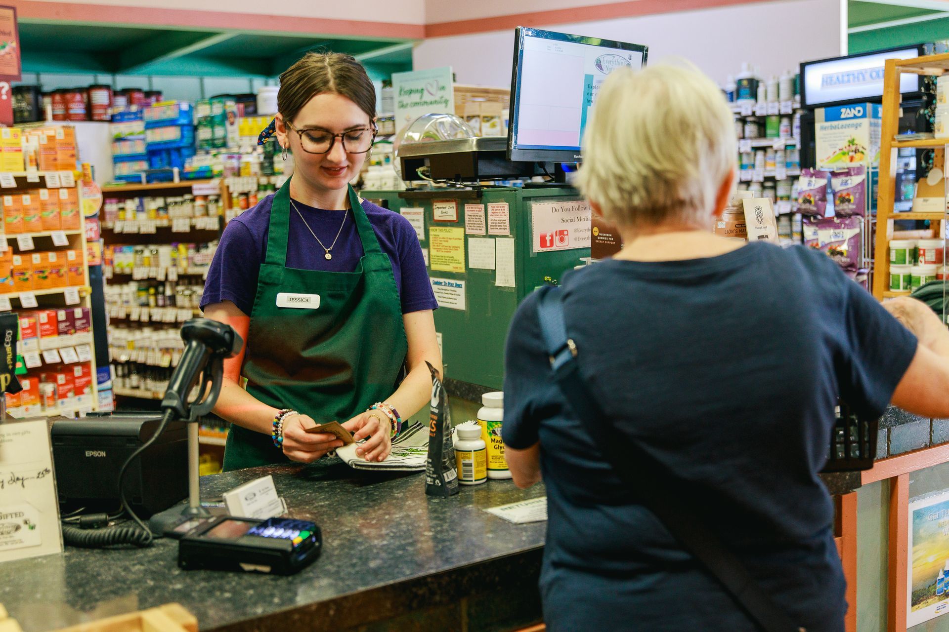 A woman is standing at a counter in a store talking to another woman.