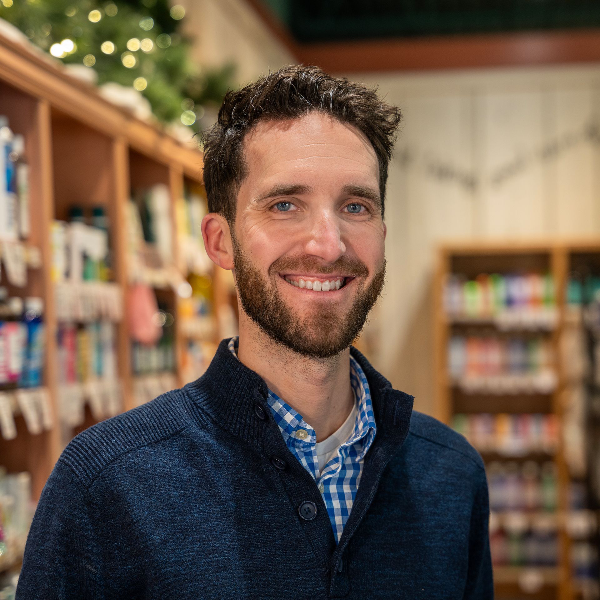 A man with a beard is smiling in front of a bookshelf in a store.