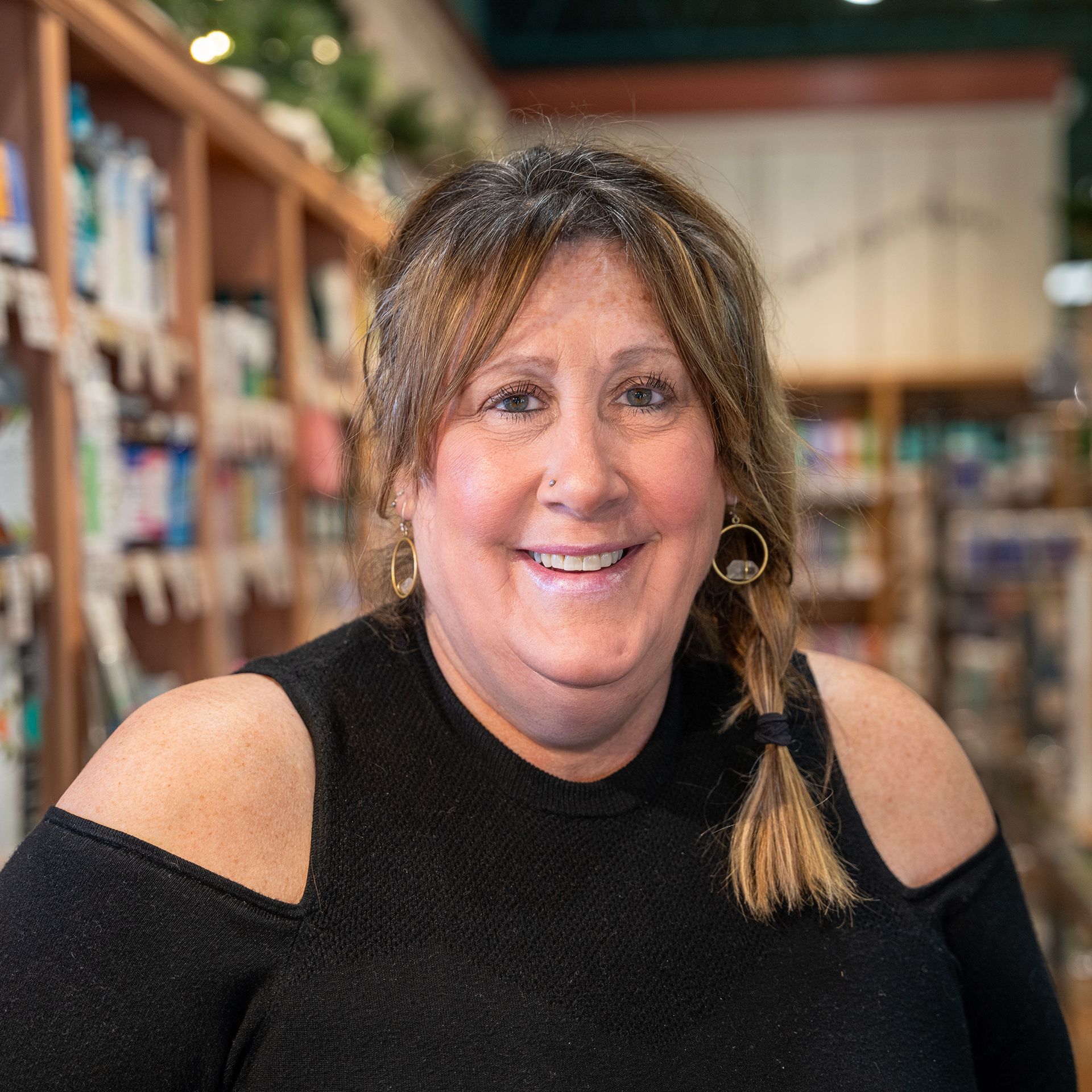 A woman in a black sweater is smiling in front of a bookshelf.