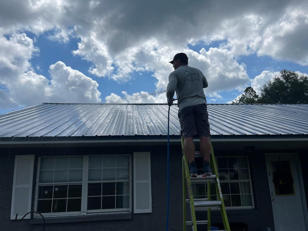 man standing on ladder and cleaning house metal roof with high pressure washer