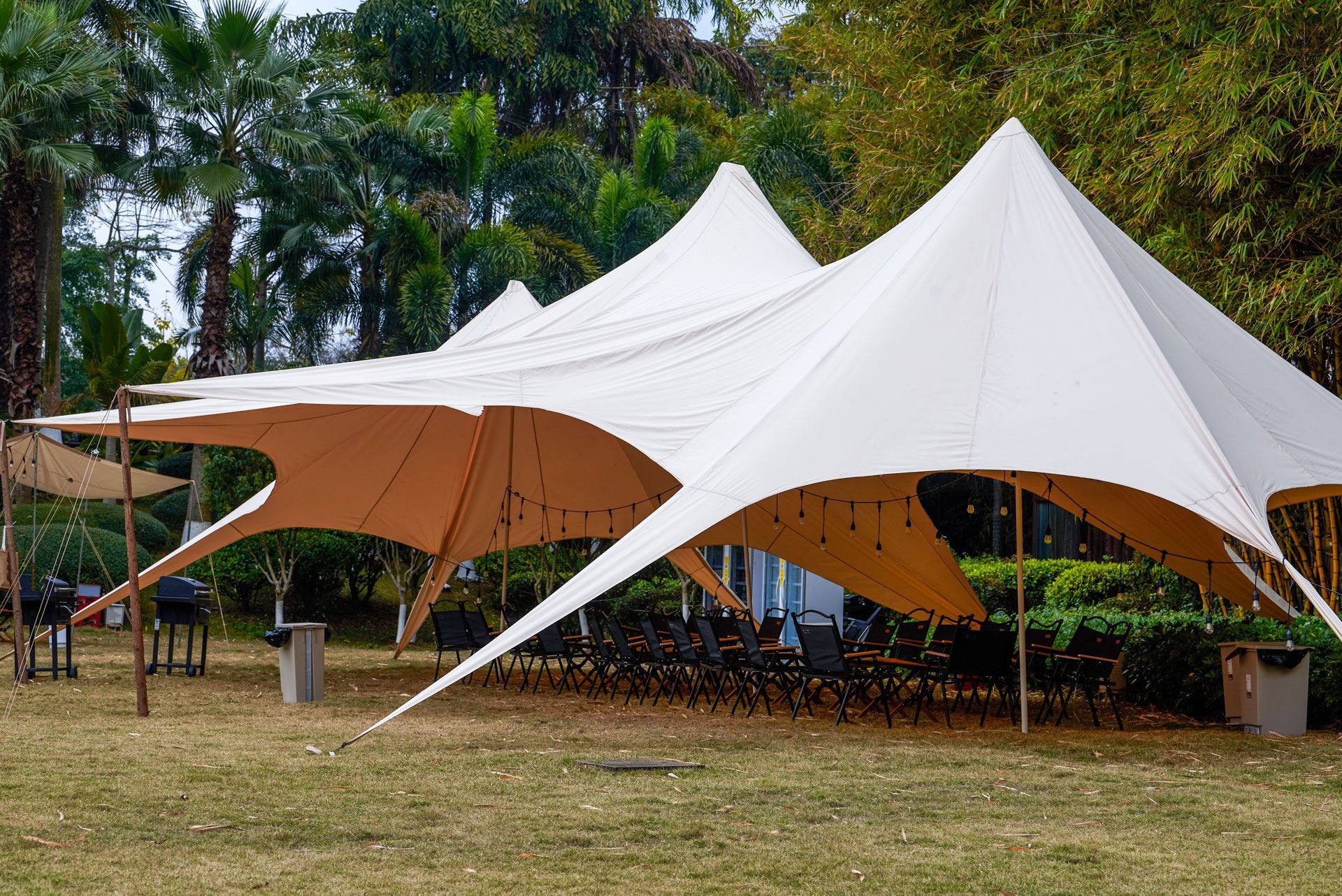 Two white canopy tents in a grassy outdoor area with trees in the background