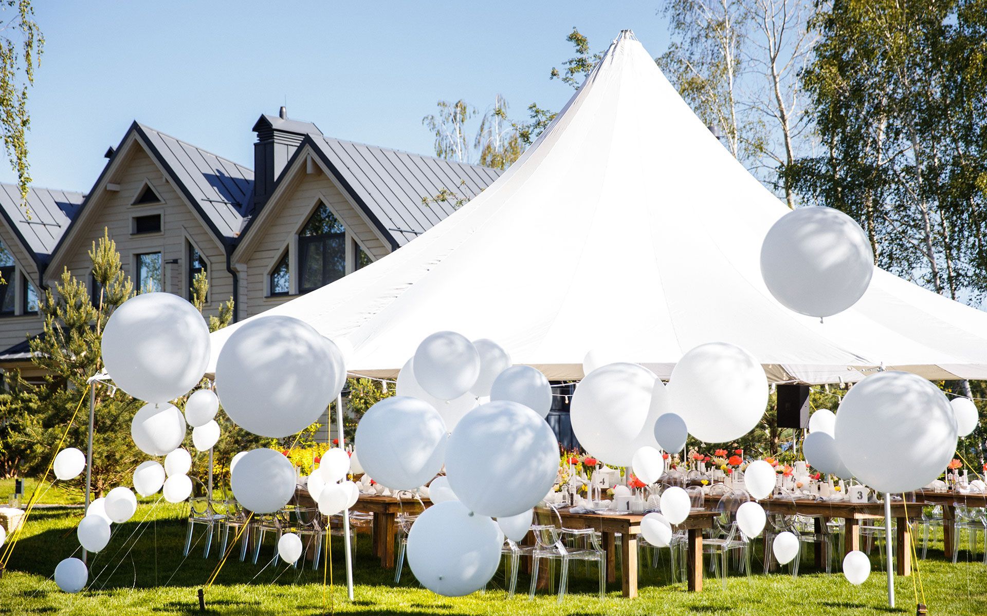 A white tent is decorated with white balloons and tables.