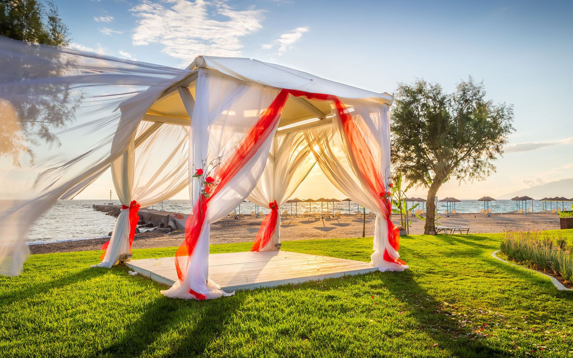 A white gazebo with red ribbons is sitting on top of a lush green field.