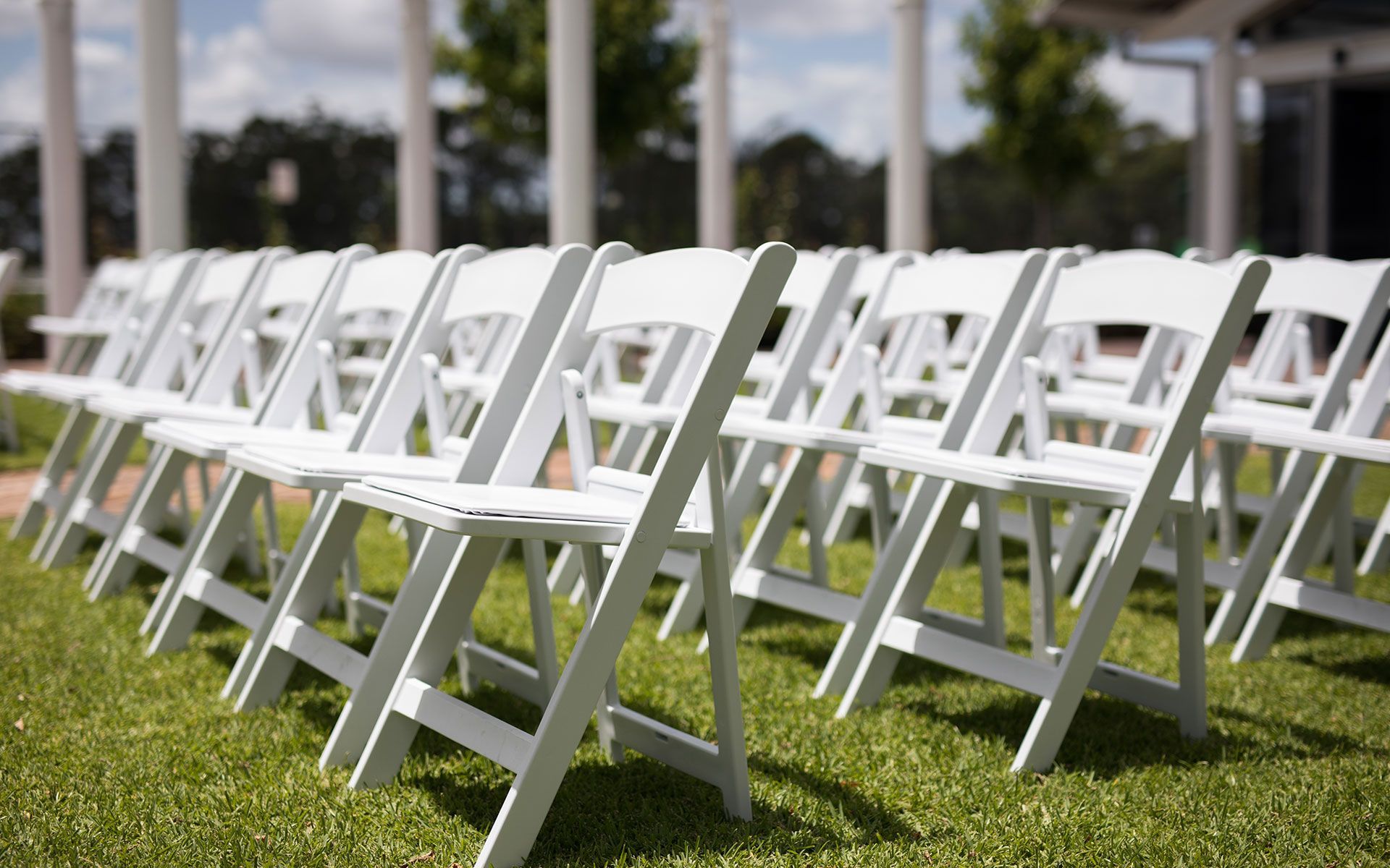A row of white folding chairs sitting on top of a lush green field.