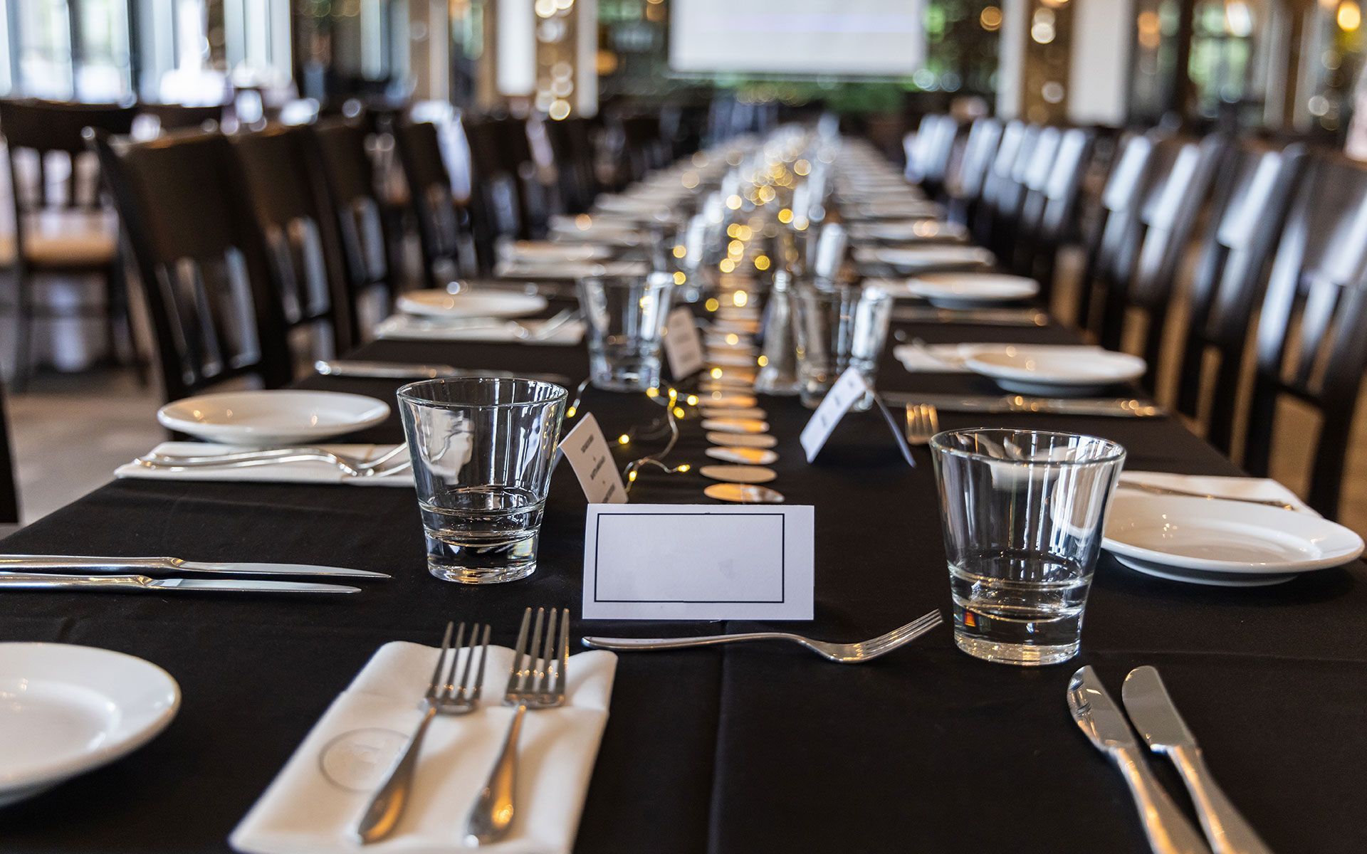 A long table with plates , glasses , silverware and a place card on it.