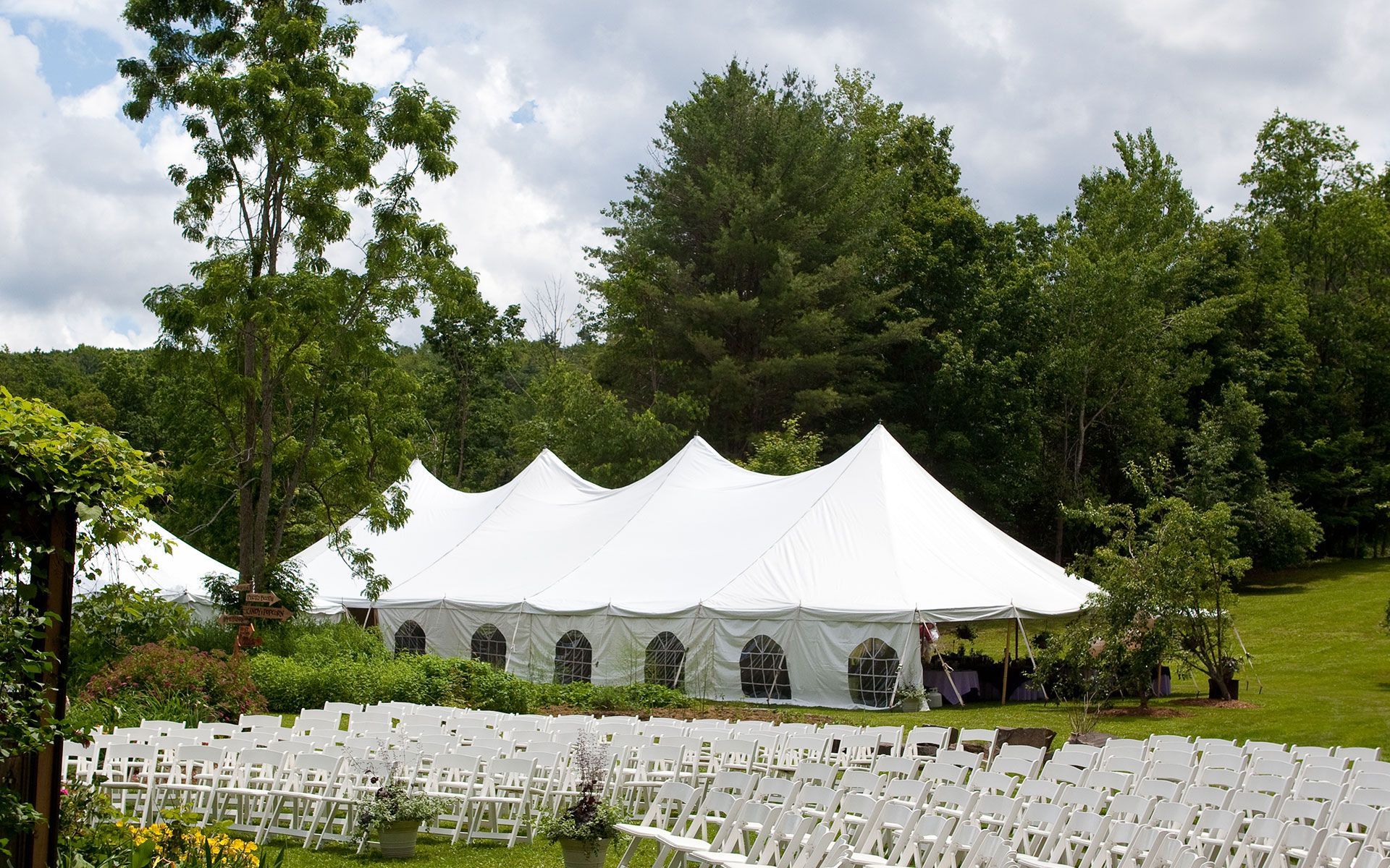 A row of white chairs are lined up in front of a large white tent.