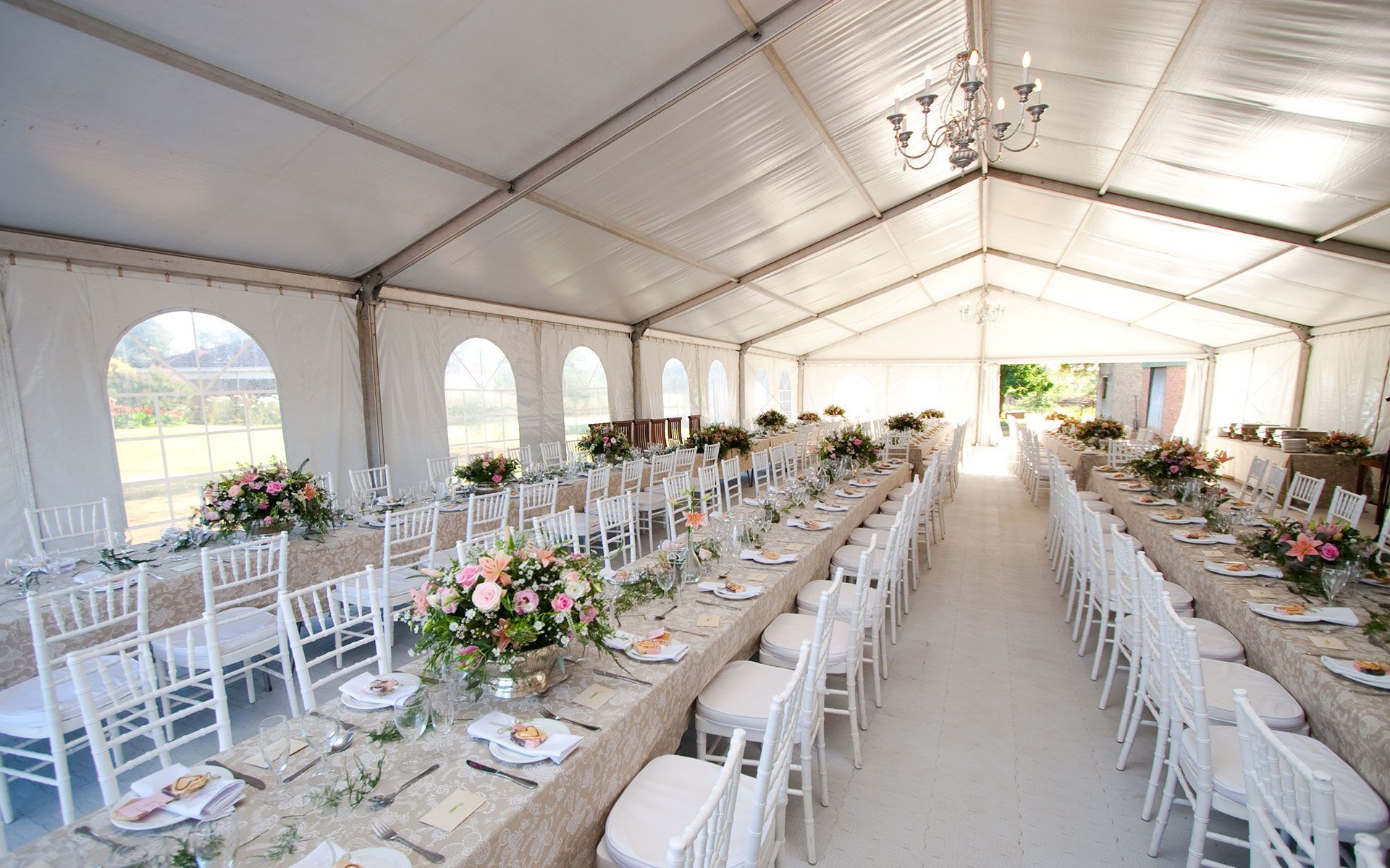 A long table and chairs are set up in a tent for a wedding reception.