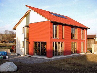 Modernes rot-weißes Haus mit schrägem Dach und großen Fenstern in ländlicher Umgebung