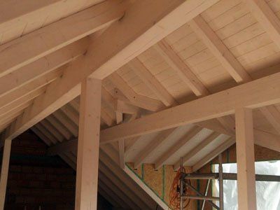 Holzvertäfeltes Dachgeschoss mit freiliegenden Balken, schräger Decke und einer Leiteröffnung auf der rechten Seite.