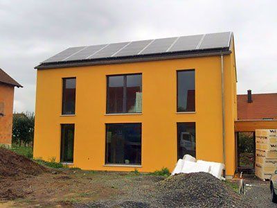 Gelbes zweistöckiges Haus mit Solarpaneelen auf dem Dach und unbebautem Grundstück drumherum