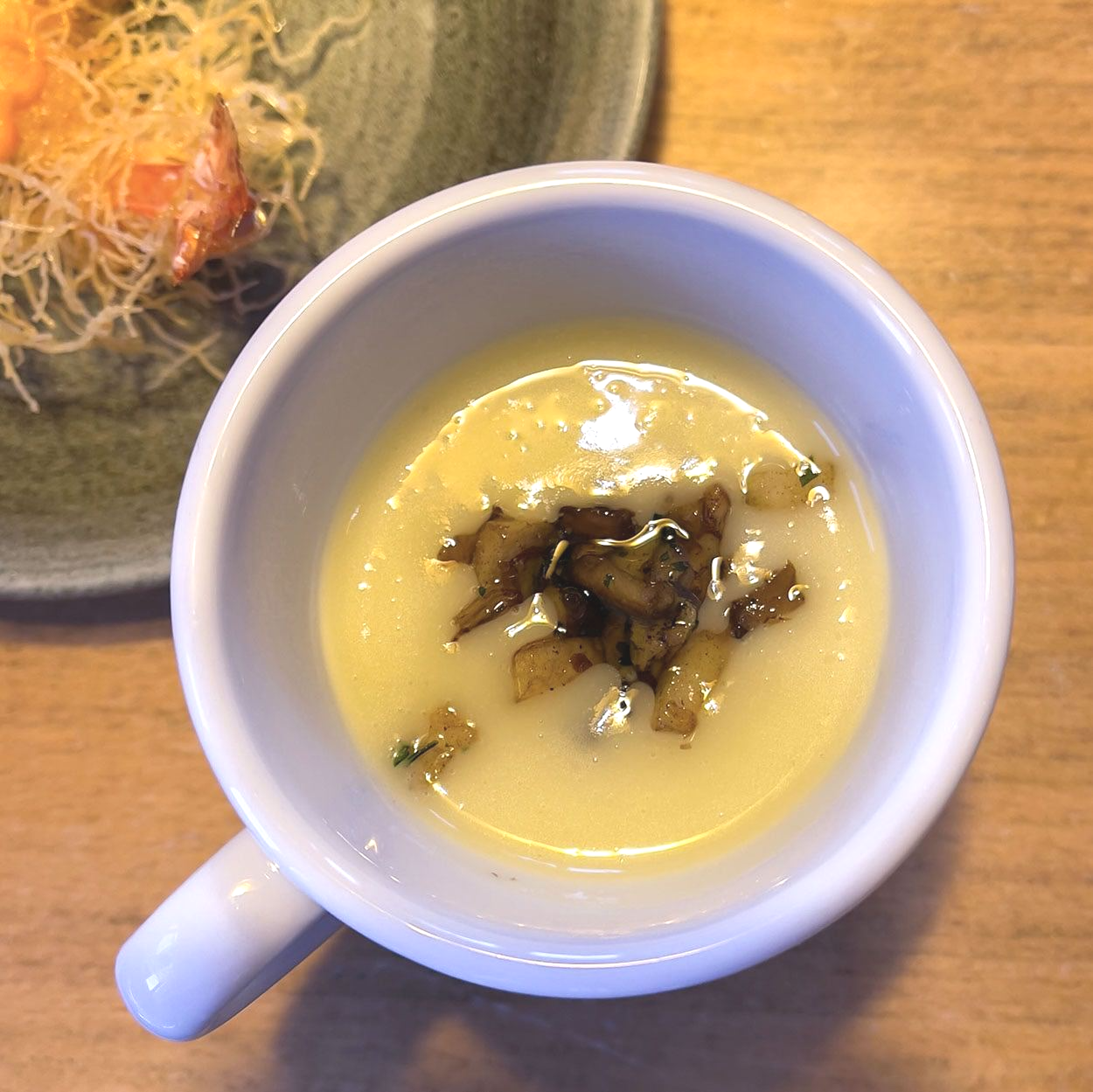 Eine Tasse Suppe mit einem Teller mit Essen im Hintergrund