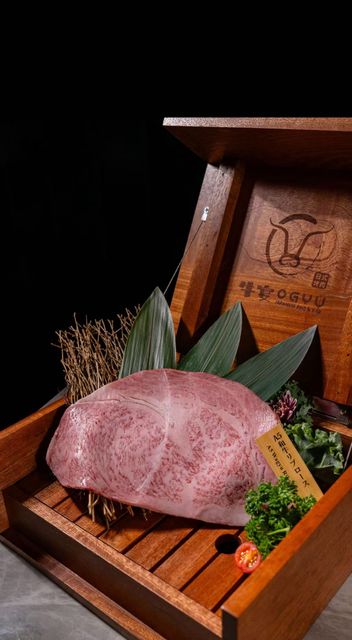 Pink dome-shaped dessert in a wooden tray with green garnish and a branded chocolate plaque