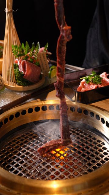 Grill with glowing coals and hanging meat over a Japanese barbecue table, with side dishes nearby