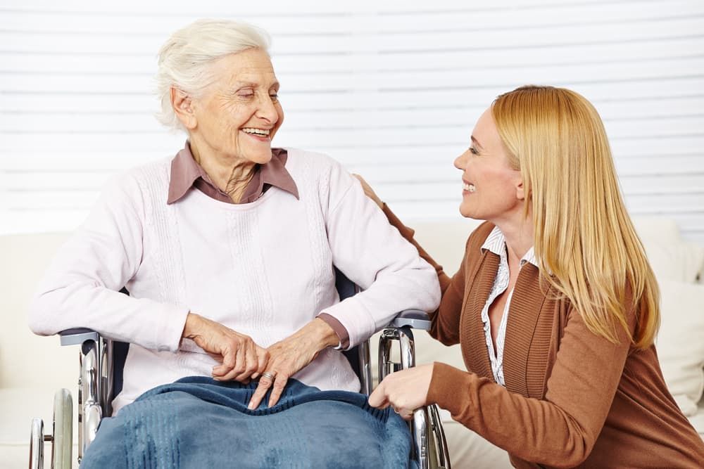 A Woman is Talking to an Elderly Woman in a Wheelchair — Empowering You Disability Services In Maryborough, QLD