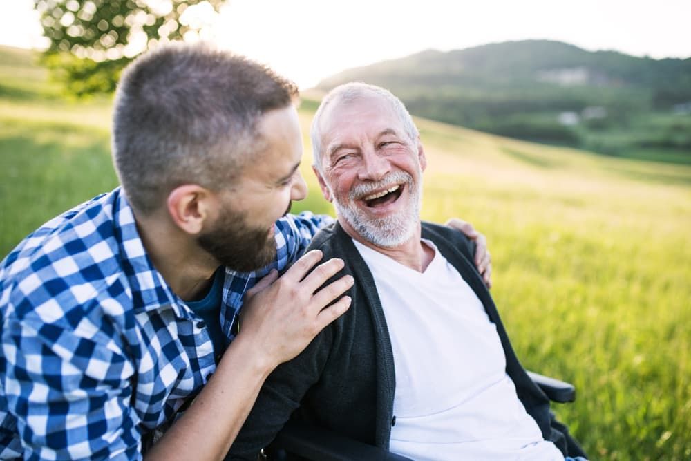 A Young Man is Talking to an Older Man in a Wheelchair — Empowering You Disability Services In Maryborough, QLD