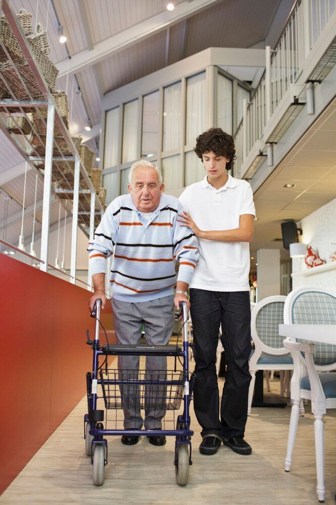 A Young Man is Helping an Older Man With a Walker — Empowering You Disability Services In Maryborough, QLD