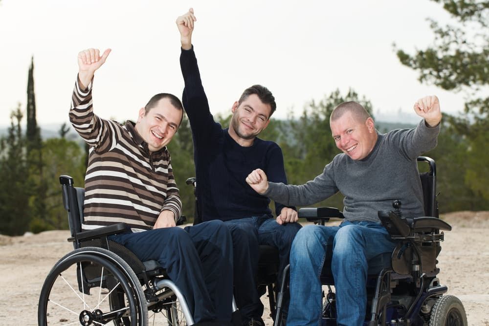 Three Men Are Sitting in Wheelchairs With Their Arms in the Air — Empowering You Disability Services In Maryborough, QLD