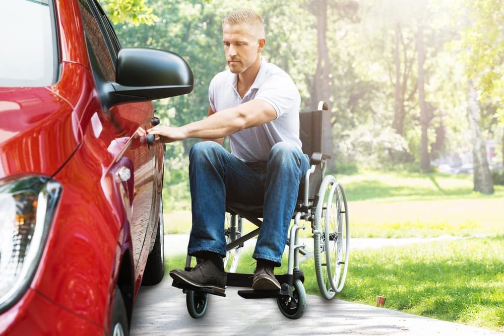 A Man in a Wheelchair is Getting Into a Red Car — Empowering You Disability Services In Maryborough, QLD