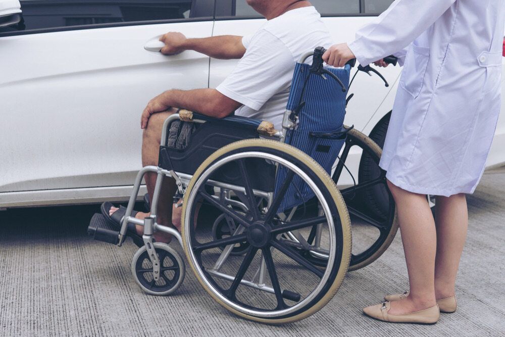 A Nurse is Helping a Man in a Wheelchair Get Into a Car — Empowering You Disability Services In Maryborough, QLD