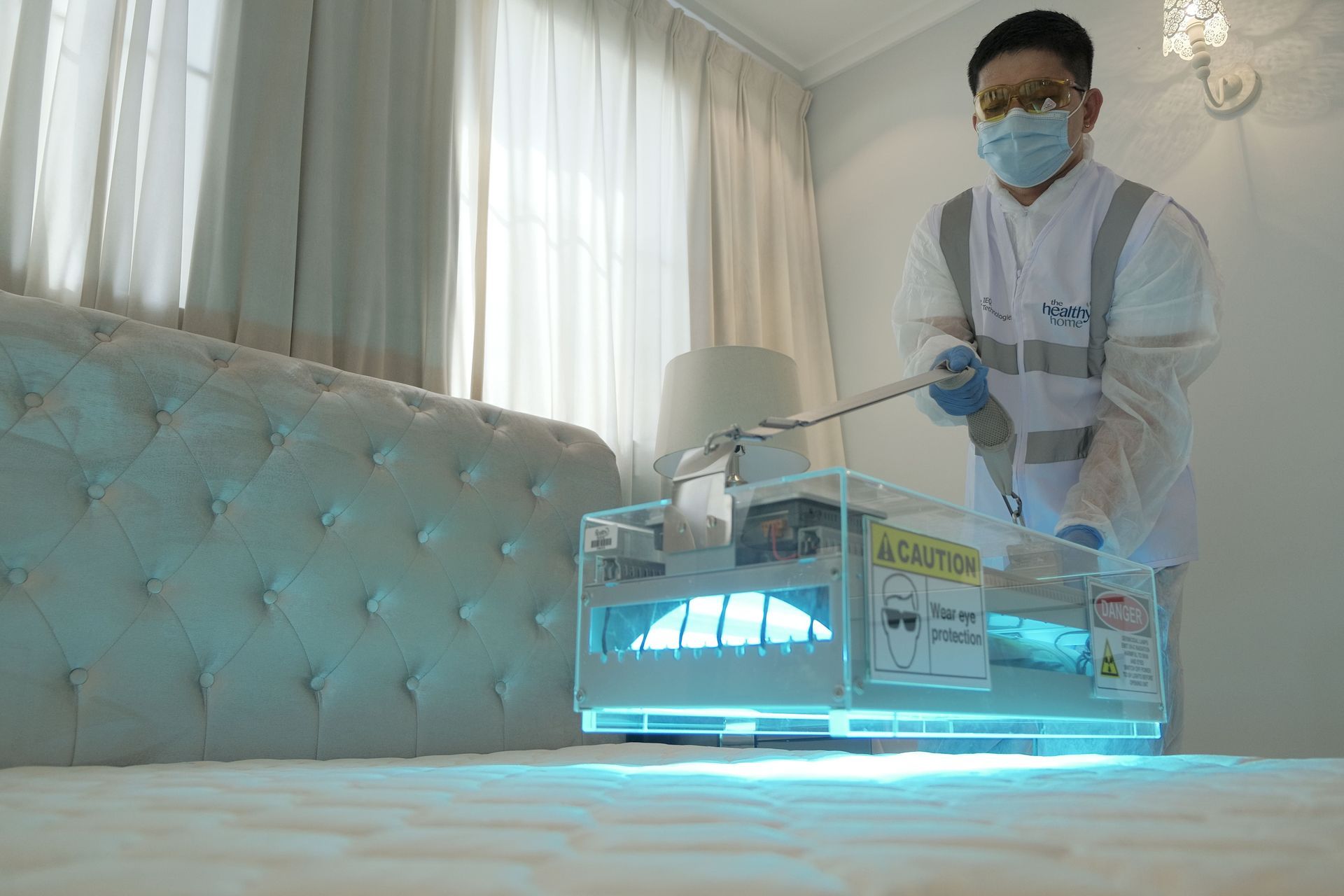 Worker in protective gear disinfecting a bright bedroom with a UV sanitizing machine