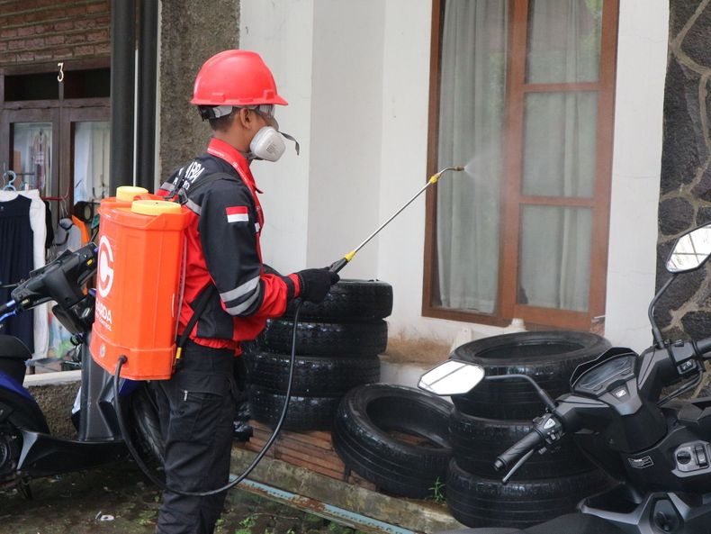 Pest control worker spraying insecticide along the floor beside a cabinet.