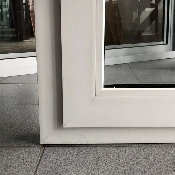 Primer plano de la esquina de una puerta de cristal con marco blanco sobre un suelo de baldosas grises.