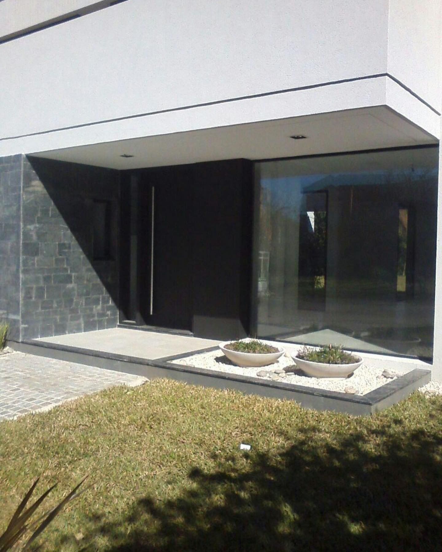 Entrada moderna al edificio con puerta negra, gran ventanal y pequeñas jardineras.