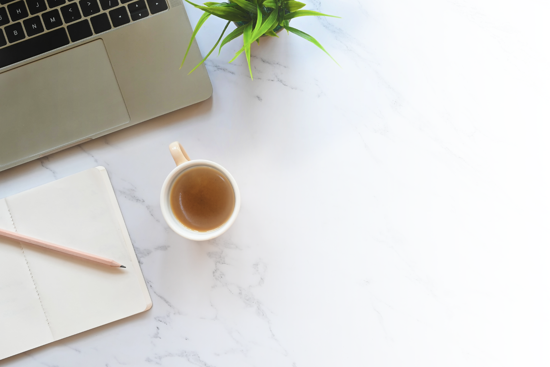 A laptop , a cup of coffee , a notebook and a pencil on a table.