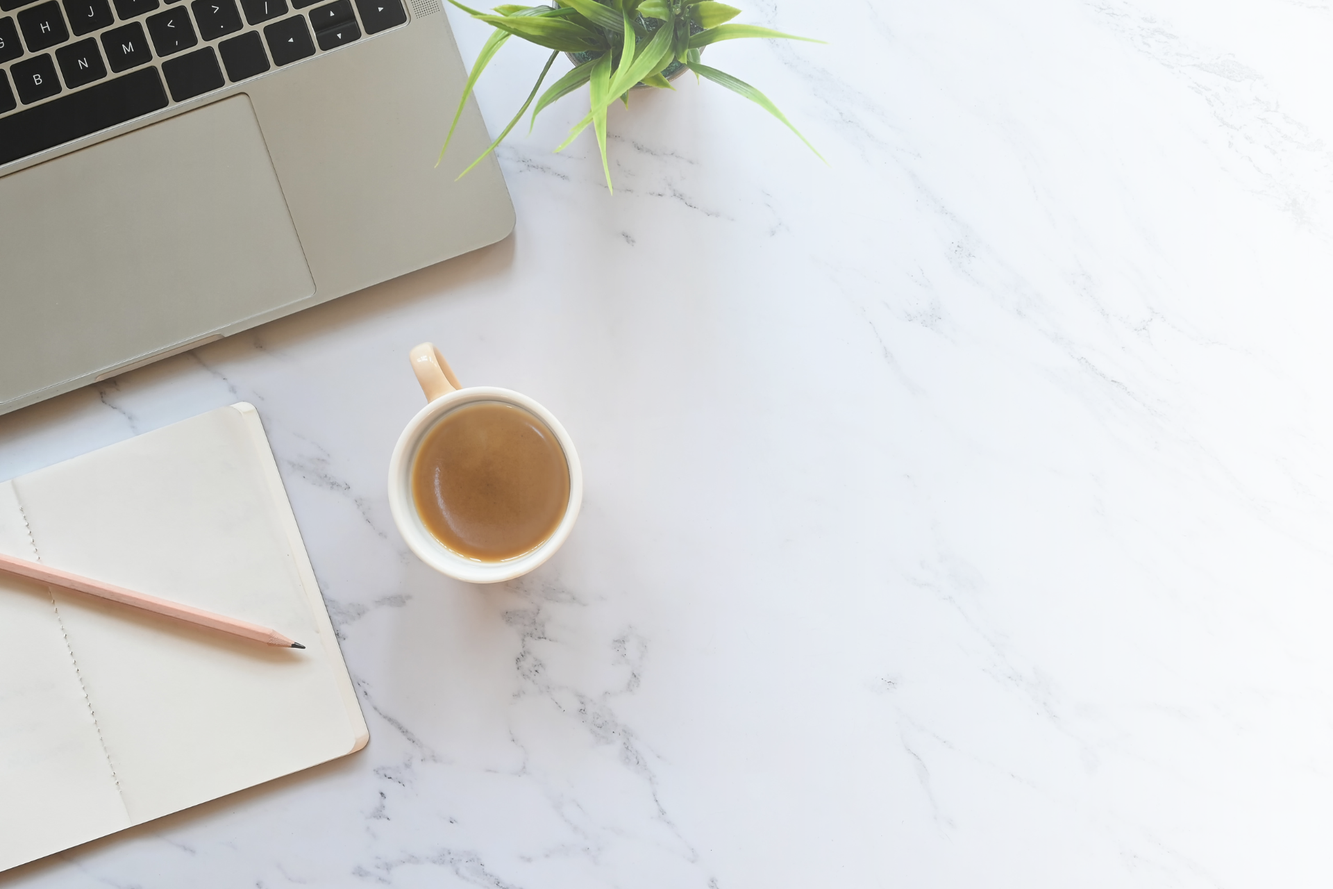 A laptop , a cup of coffee , a notebook and a pencil are on a table.